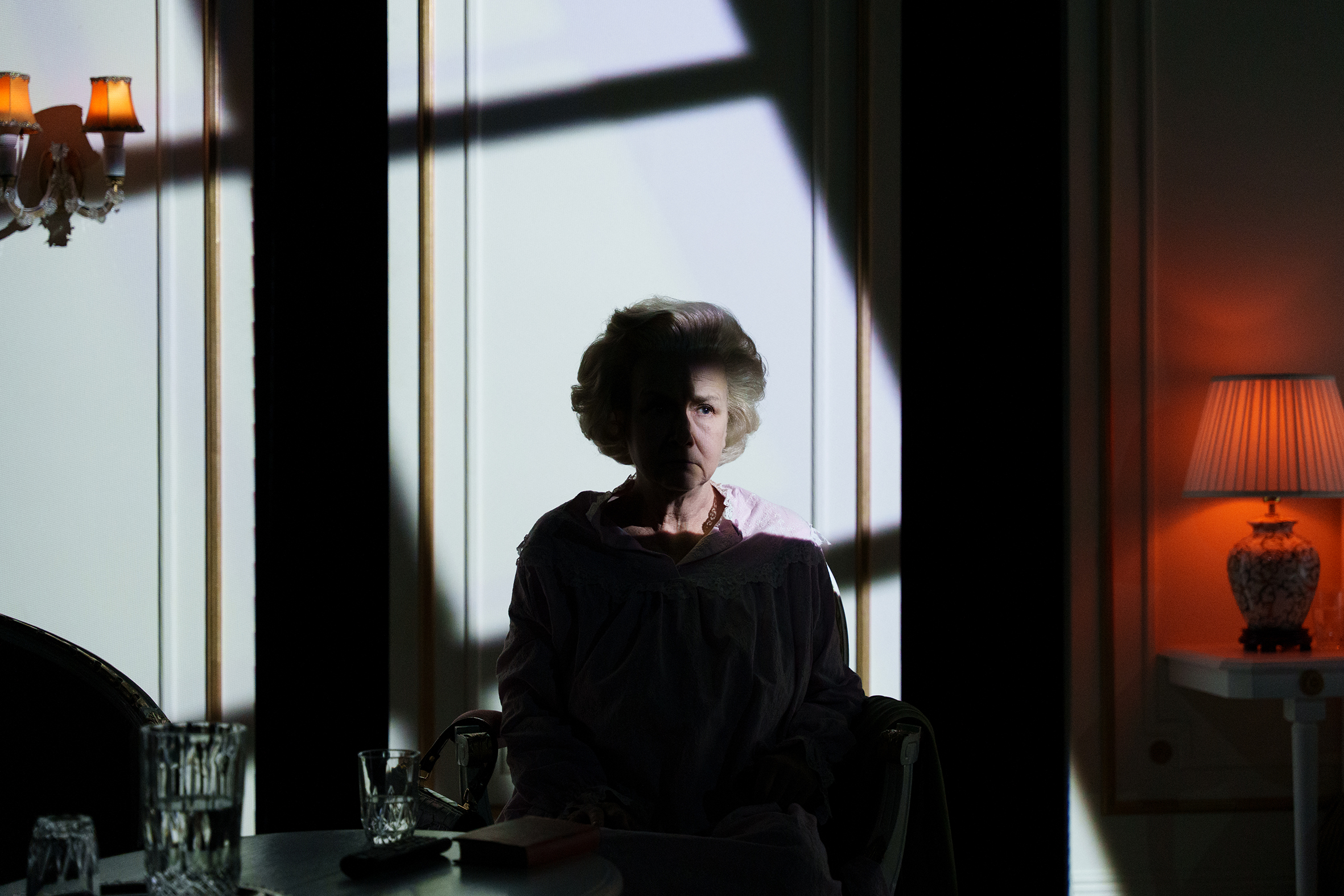 Kuvassa on tummia heijasteitä, joiden välistä näkyy Paula Siimes puolivartalokuvassa istumassa puolivarjossa. Oikealla on punaista väriä.