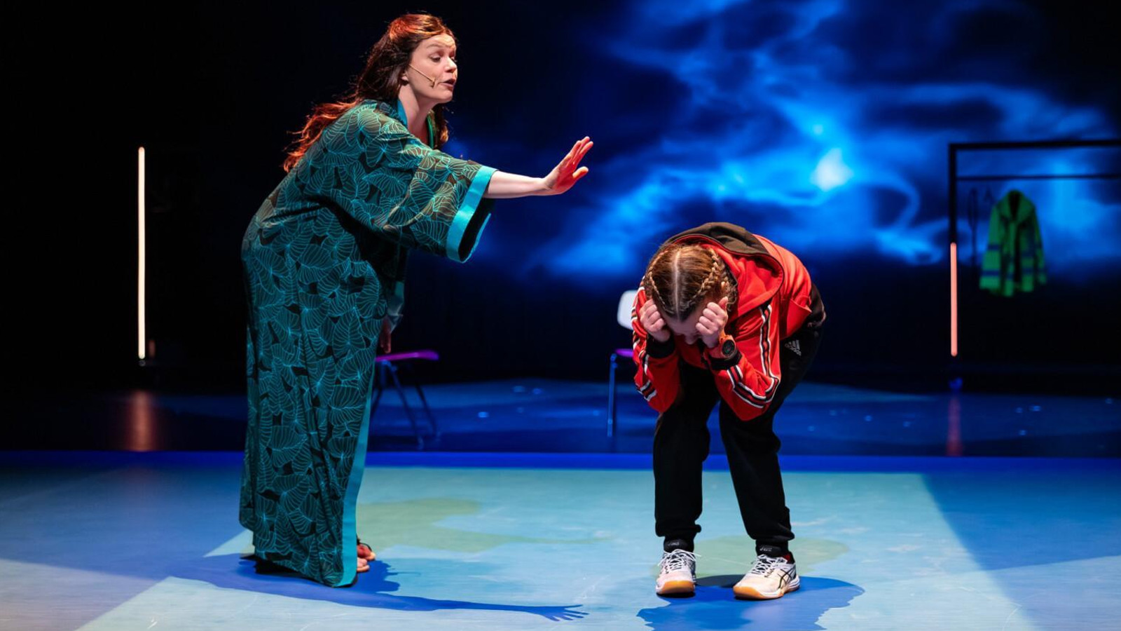 Kuvassa on vasemmalla tumman vihreässä aamutakissa sivuttain ja osoittaa oikealla kädellään tyttöä, joka on kumartuneena eteenpäin. Hän pitelee käsillään hiuksiaan.