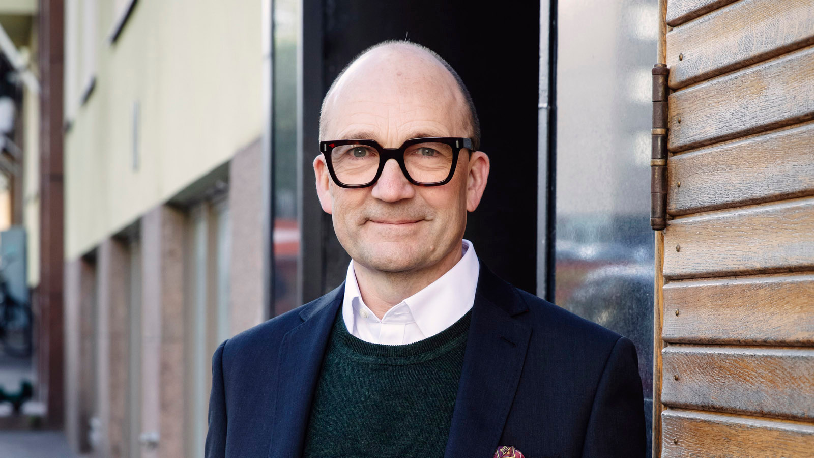 Kuvassa on Thomas de Mallet Burgess puolivartalokuvassa seisomassa. Hänellä on tumman sininen takki, tumma pusero ja valkoiset kaulukset. Taustalla on vaaleata kerrostaloa.