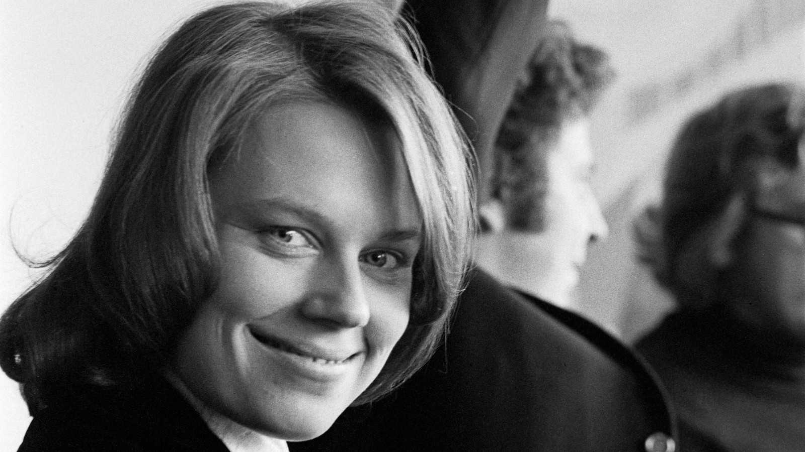 Kuvassa on Arja Saijonmaa nuorena kasvokuvass. Taustalla näkyy Mikis Theodorakis selin ja osaa kasvoista. Kuva on musta-valkoinen.