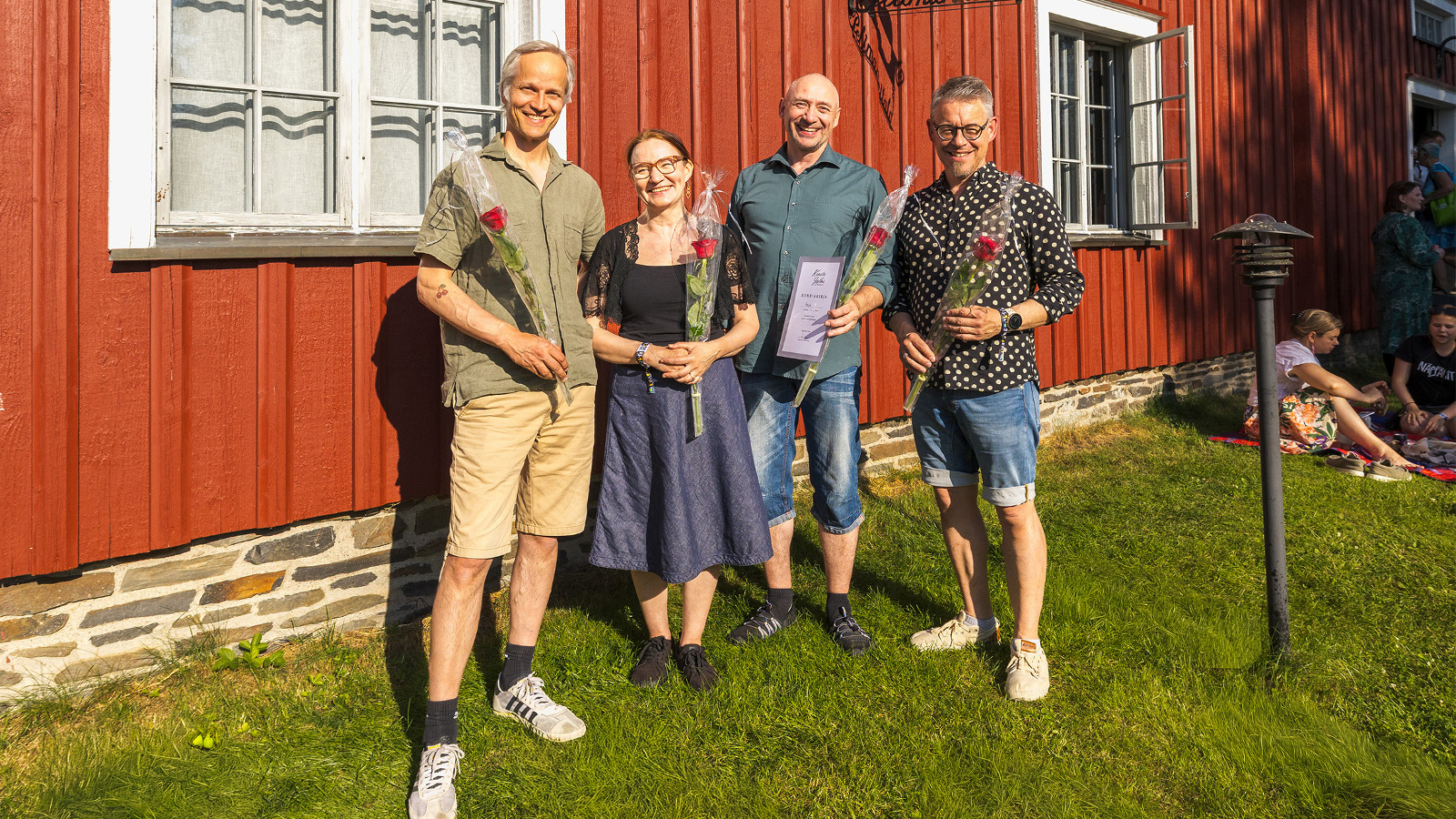 Kuvassa on yhtye Freijan neljä esiintyjää ja vasemmalla on mies, jolla on vihertävä paita ja kellertävät shortsit. Hänen oikealla puolellaan on nainen sinisessä mekossa ja mies sinisessä paidassa ja farkkushortseissa. Vasemmalla on mies valkopilkulisessa paidassa ja sinisissä farkkushortseissa. Taustalla on punainen puurakennusta ja ikkuna valkoislla ikkunanpielillä.