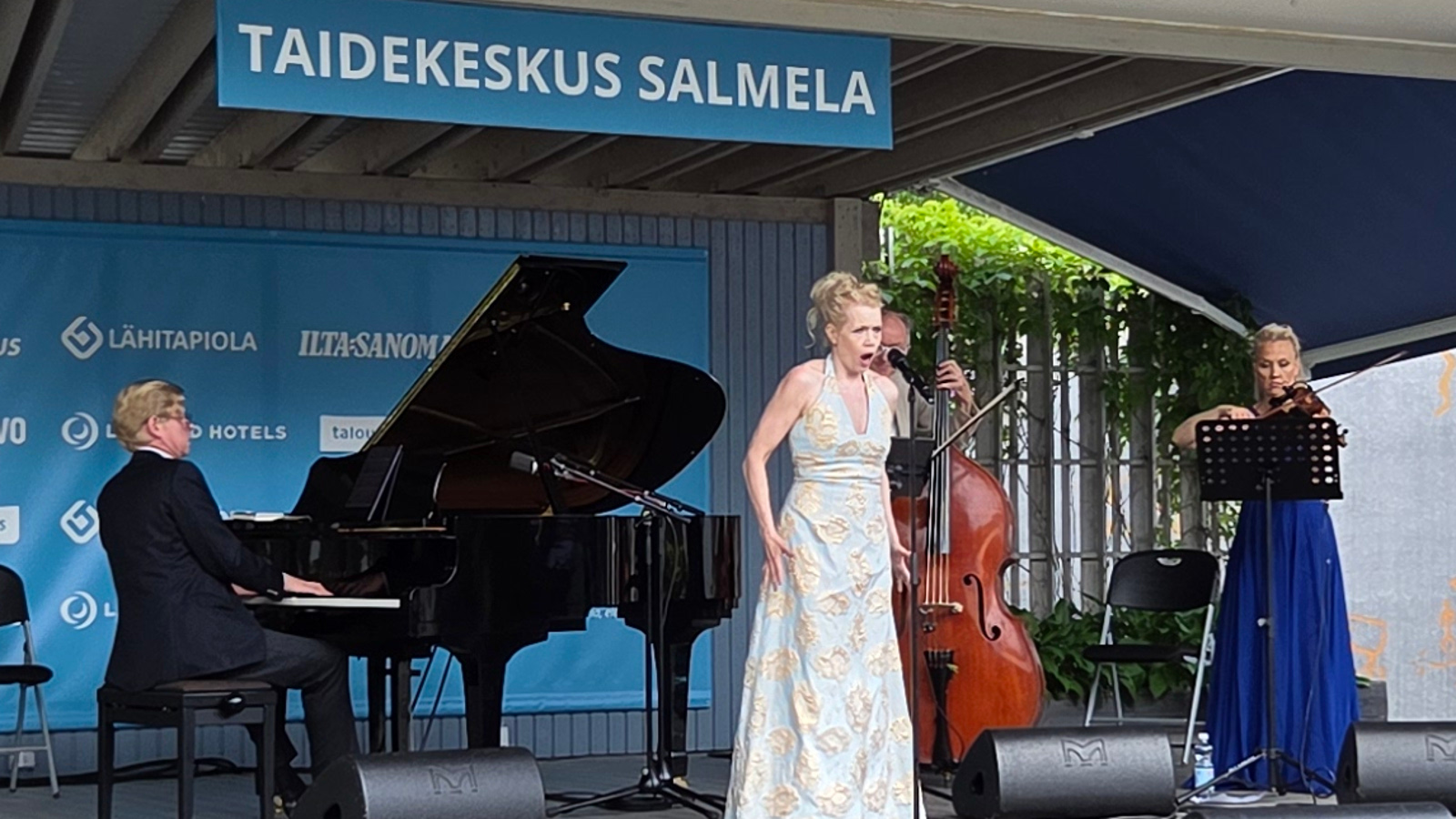 Kuvasswa on Kuvassa on vasemmalla Janne Hovi soittamassa flyygeliä ja keskellä Helena Juntunen vaaleassa, pitkässä puvussa laulamassa. Takana soittaa kontrabassoa Hannu Rantanen takana ja oikealla Maija Linkola viulua pitkässä, sinisessä puvussa. Päällä lukee Taidekeskus Salmela.