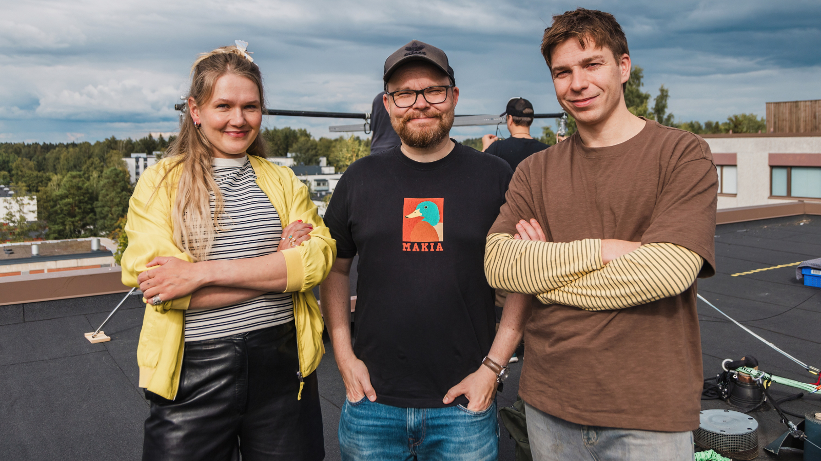 Kuvassa on puolivartalokuvassa ulkona vasemmalla Milla Virtanen keltaisessa villatakissa ja keskellä Antti Heikki Pesonen mustassa t-paidassa. Oikealla on Tom Rejström ruskeassa t-paidassa.