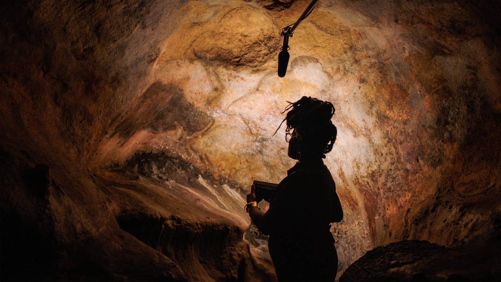 Kuvassa on ruskehtavaa luolaa ja sen keskellä on vaalea kohta. Sen udessä on tumma naishahmo.