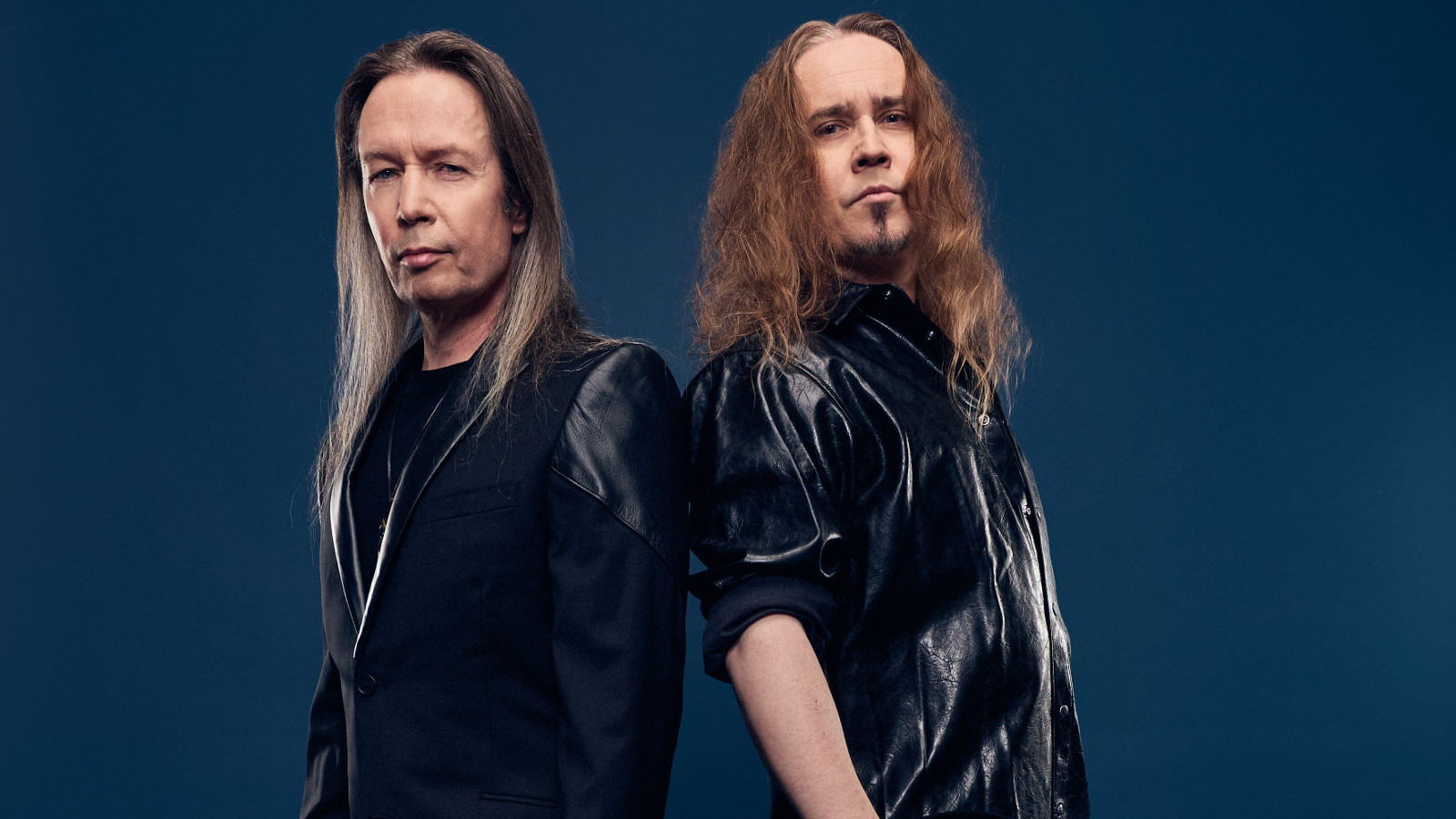 Kuvassa on vasemmalla Timo Kotipelto ja oikealla Jarkko Ahola. He ovat osittain selin ja molemmilla on mustat puserot ja pitkät hiukset.