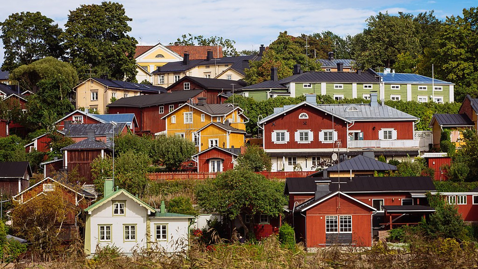 Kuvassa on vanhan Porvoon rinnettä ja siinä olevia taloja, jotka ovat eri värisiä.  Kuva on otettu kesällä aurinkoisella ilmalla.