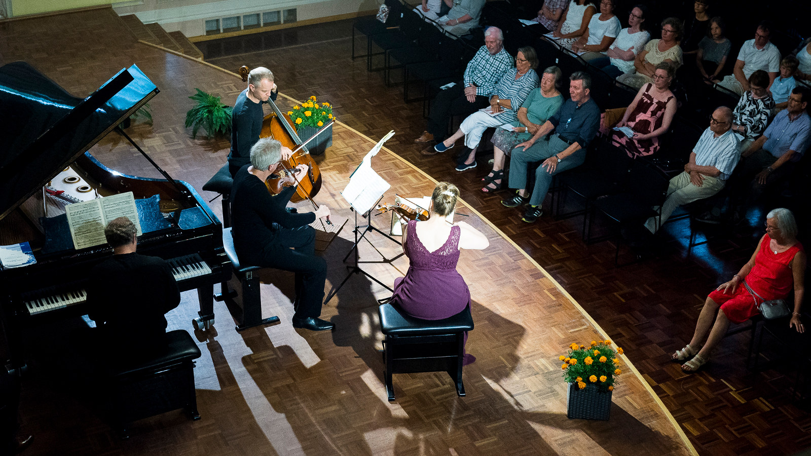 Kuvassa on Faure Quartet ja kuva on otettu ylhäältä päin. Vasemmalla on flyygeli soittajineen ja lavalla on vasemmalla sellistimies mustissa vaatteissa, miesviulisti ja oikealla istuu lilassa hameessa oleva naisviulisti.  Alempana näkyy yleisöä istumassa.