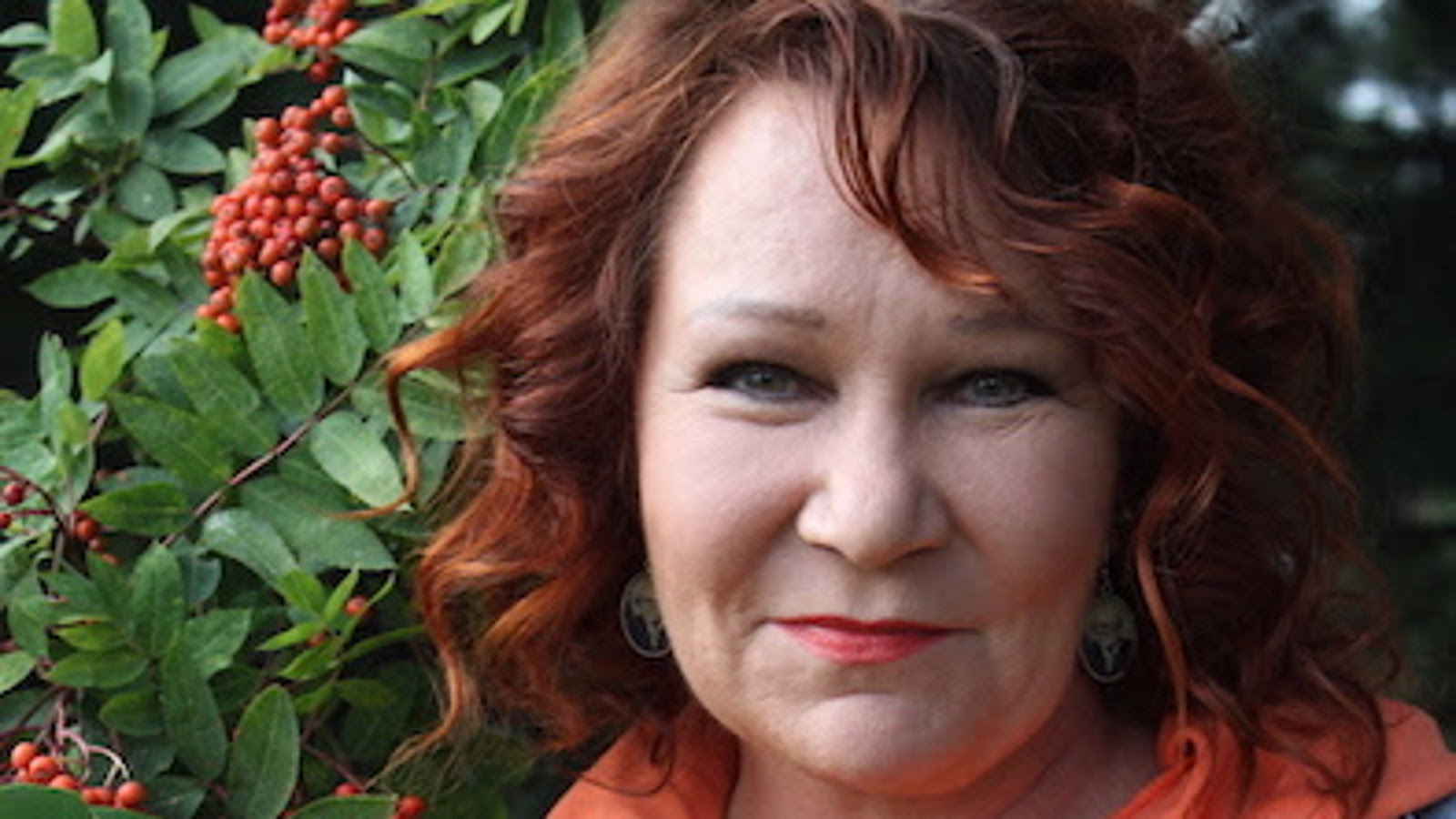 Kuva on Vicky Rostista, jolla on punaiset hiukset. Taustalla vasemmalla on vihreitä pihlajan lehtiä ja oransseja pihlajanmarjoja.  Kuva on kasvokuva. 