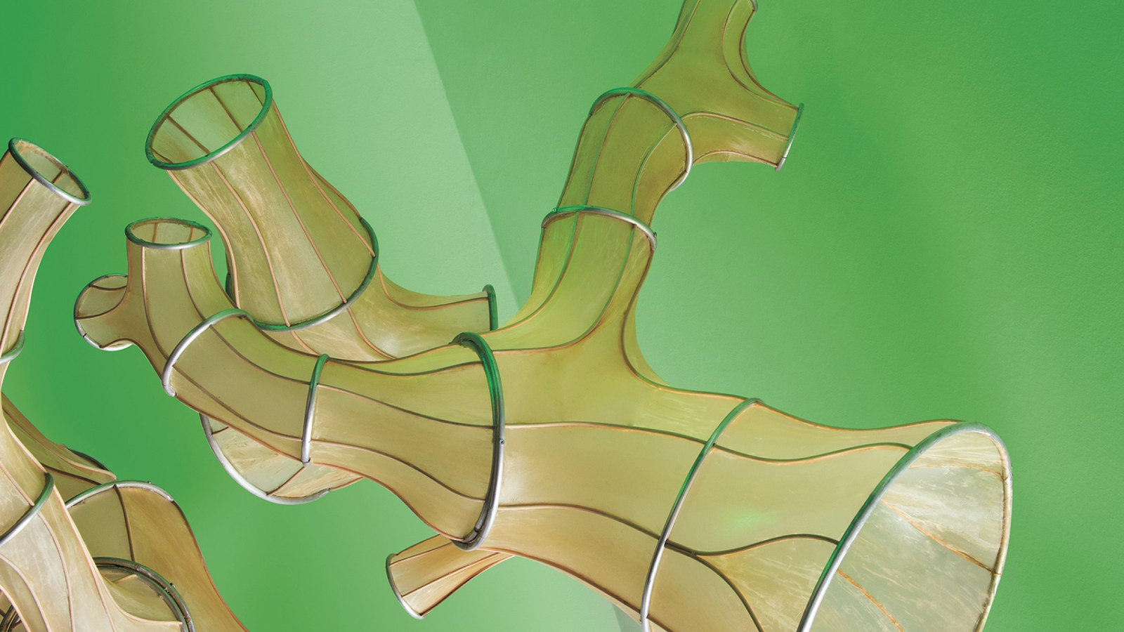 Kuvassa on Julia Lohmanin installaatio Okinaganode sculpture, jossa vaalean vihreällä pohjalla kelluu vaalean ruskeita putkilomaisia teoksia. Pinnassa on muutamia renkaita ja pituussuuntaisia juovia.
