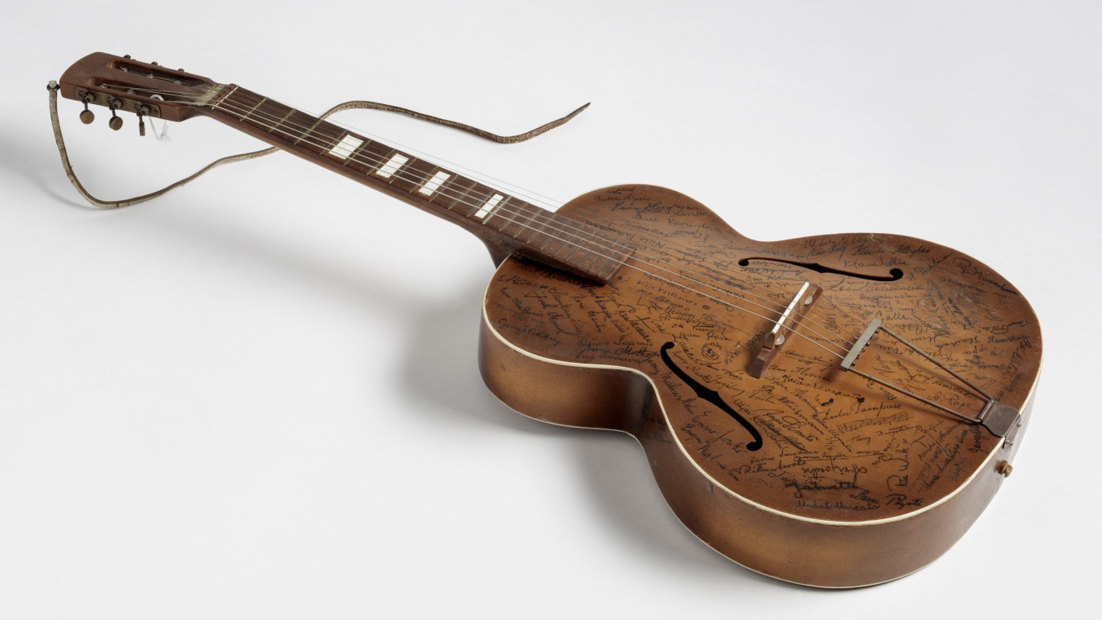 Kuvassa on Reino Helsimaan kitara, jossa on kannessa runsaati nimikirjoituksia.  