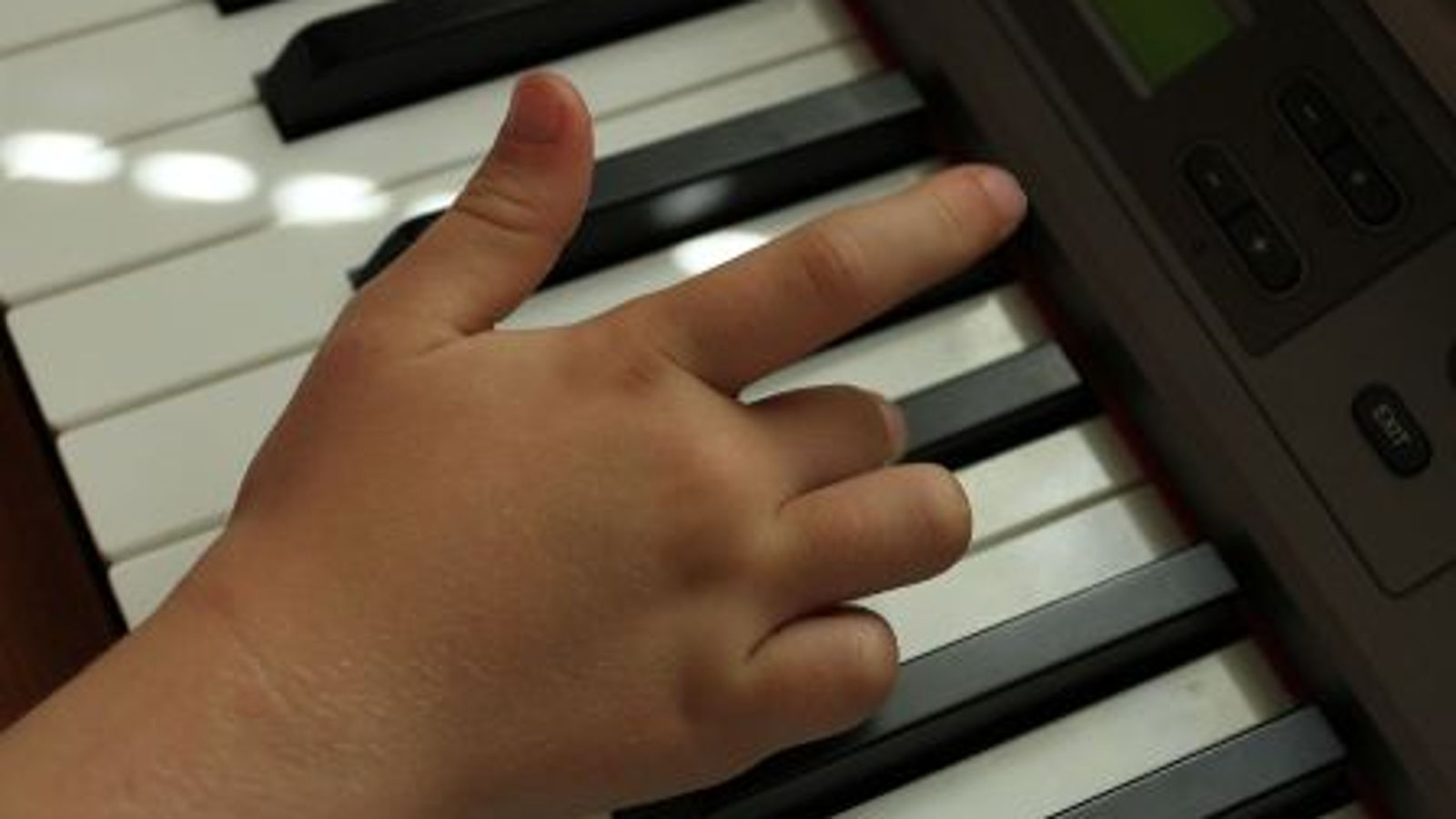 Kuvassa on lapsen käsi pianon koskettimilla ja soittaja tapailee valkoisia koskettimia. 