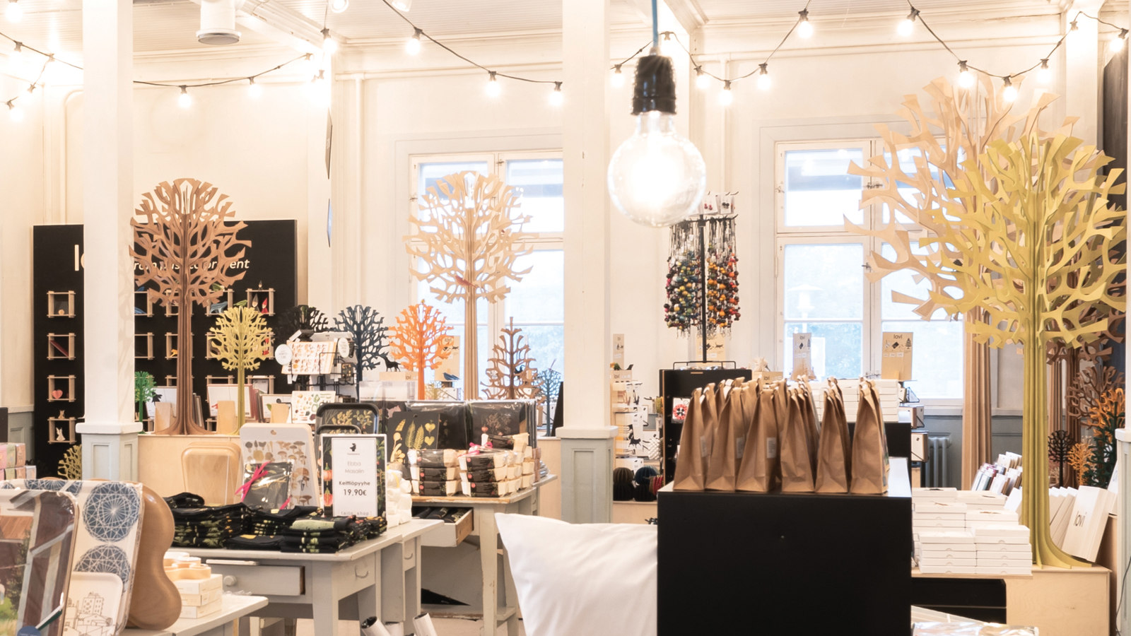 Kuvassa on Oulun Taito-shop -myymälä ja siinä on esillä erilaisia käsityötuotteita sekä puusta tehtyjä puita. Myymälä on kauniisti valaistu ja ilmeeltään valoisa.   
