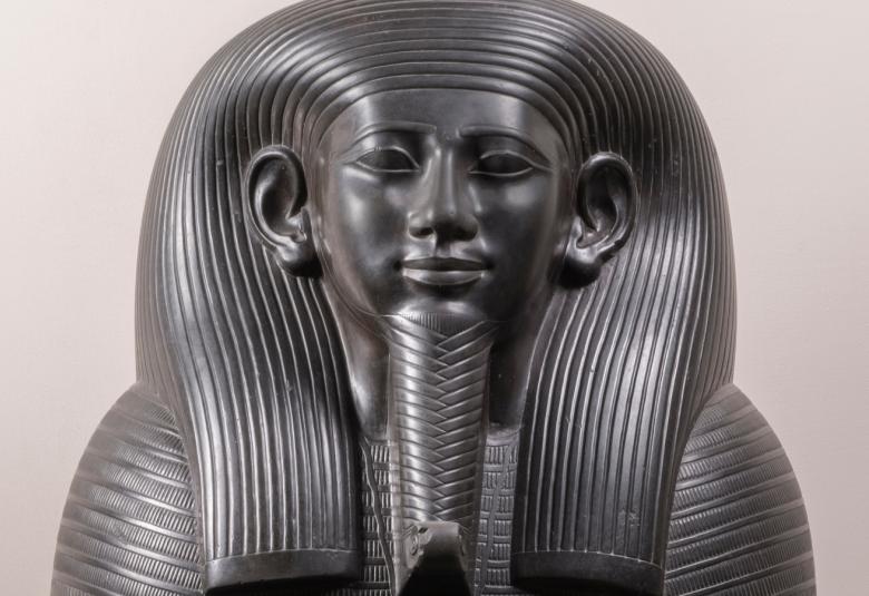 Kuvassa on sargofagin kansi ja siinä olevan muumion pään kuva. Pää on tumma ja tausta harmaa.