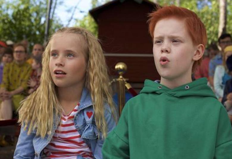 Kuvassa vasemmalla on Lumi Kallio , jolla on vaalea krepattu tukka ja päällään vaalean sininen farkkutakki sekä valko-punainen t-paita. Oikealla on Silmu Ståhlberg, jolla on punainen tukka ja päällään vihderä huppari.  Taustalla on yleisöä istumassa ulkoilmatilaisuudessa. 