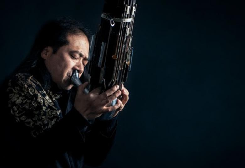 Kuvassa on Wu Wei, joka soittaa sheng-soitinta.  Soittimessa on pitkä suukappale ja soitin kaartuu ylöspäin lähesneliskulmaisen muotoisena.  Kuvan tausta on tumma ja kuvassa korostuvat soittajan kasvot ja kädet.  Puvusta näkyy osa hartiaa ja väri on kultakuvioinen mustalla pohjalla. 