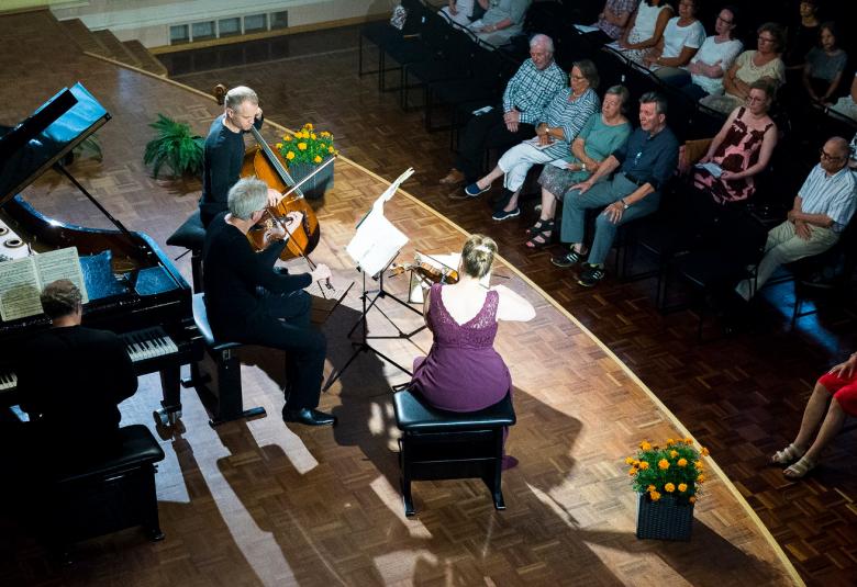 Kuvassa on Faure Quartet ja kuva on otettu ylhäältä päin. Vasemmalla on flyygeli soittajineen ja lavalla on vasemmalla sellistimies mustissa vaatteissa, miesviulisti ja oikealla istuu lilassa hameessa oleva naisviulisti.  Alempana näkyy yleisöä istumassa.