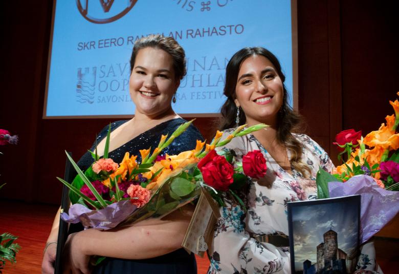 Kuvassa vasemmalla Sonja Herranen kädessään oranssisävyiset kukat ja päällään tumma, avokaulainen mekko ja ruskeat hiukset taakse kammattuna. Vasemalla on Iris Candeleria kädessään kukat ja Olavinlinnan kuvalla varustettu palkintokirja. Hänellä on päällään mekko, jossa on valkoisella pohjalla sinisiä kukkia. Takana on kilpailun tunnus, jossa on Suomen kulttuurirahaston ja Eero Rantalan Säätiön logot.