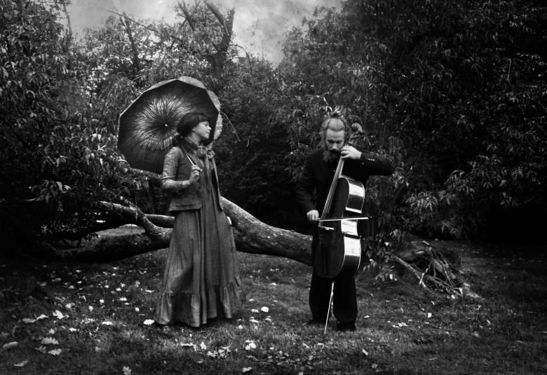 Kuva on musta-valkoinen kuva Sagolik duosta.  Stina Koistinen on vasemmalla ja Juho Kanorvo oikealla. He ovat metsässä kaatuneen puun edessä.  Koistisella on päällään tumman harmaa rimpsuhelmainen pitkä hame ja jakku sekä päivänvarjo.  Kanervo soittaa selloa ja on pukeutuneena mustaan pukuun. 