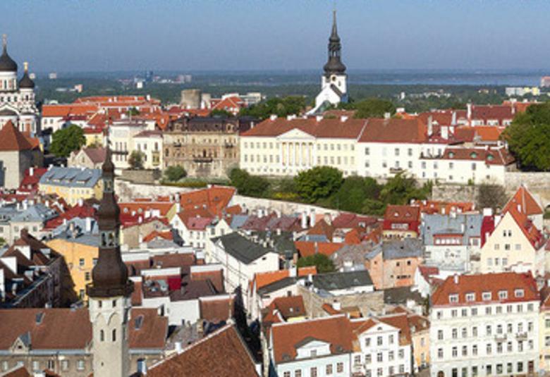 Kuvassa on Tallinnan vanhankaupungin kattoja ja rakennuksia kuvattuna ilmasta.  Kuva on otettu aurinkoisena päivänä  ylimpänä näkyy sinistä taivasta.