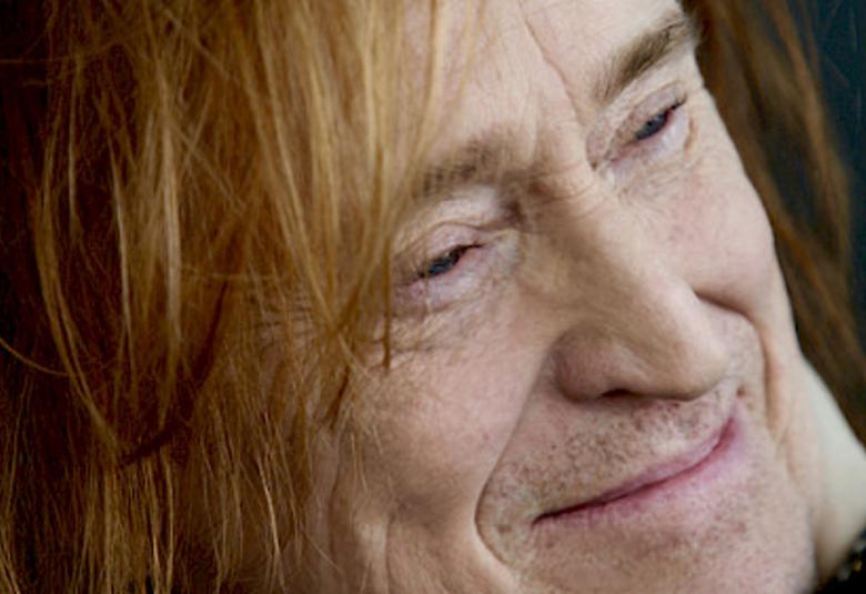 Kuvassa on Tommi Läntisen kasvot ja katse oikealle. Hänellä on punaiset hiukset ja hymyilee. Tausta on musta.