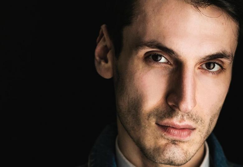 Kuvassa on Pajtim Statovci ja hänestä on kasvokuva.  Hän katsoo suoraan kameraan ja on tumma tukkainen.  Kuvassa näkyy vaalea kauluspaita ja tausta on tumma.