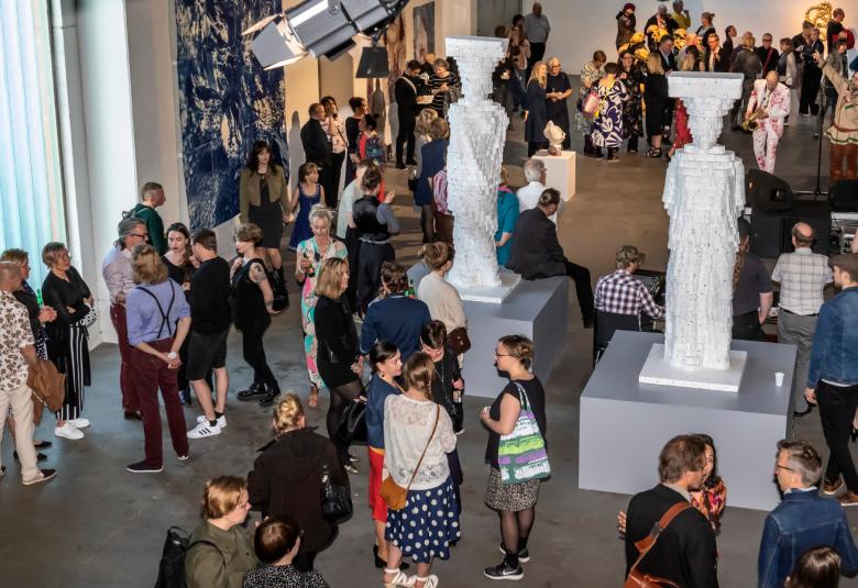 Kuvassa on ylhäältä päin kuvattu yleisöä Pekilossa Mäntässä.  Yleisöä on koko salin alalla pienissä ryhmissä keskustelemassa.  Salissa on valkoisia isoja patsaita.