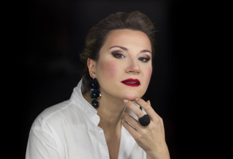 Kuvassa on Ekaterina Gubanova ja hänellä on lyhyet, tummat hiukset.  Kuvassa  näkyy roikkuva tummista pyörylöistä koostuva korvakoru sekä vasemmassa kädessä keskisormessa musta pyöreä iso sormus.  Gubanova pitää kättään kevyesti leuassa.  Kuva on puolivartalokuva ja hänellä on valkoinen paitapusero päällään. Kuvan tausta on musta.