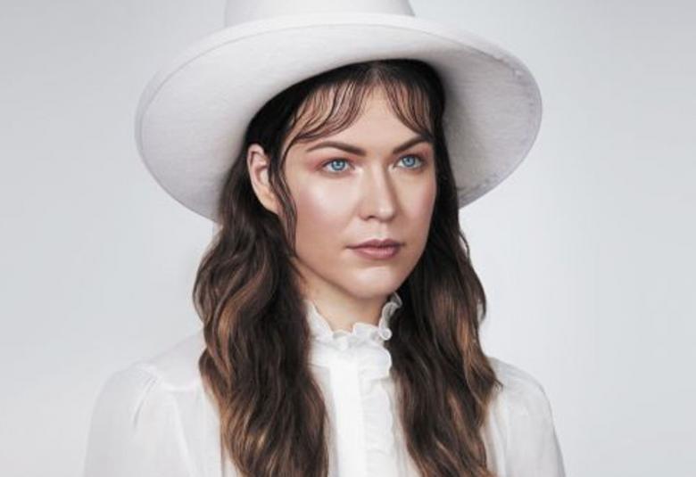 Kuvassa on Jenni Vartiainen valkoinen stetson-hatu päässään. Kuvan tausta on harmahtavan valkoinen.  Vartiaisen katse on vinosti oikealle ja tummat pitkät hiukset.  Päällään hänellä on valkoinen paitapusero.