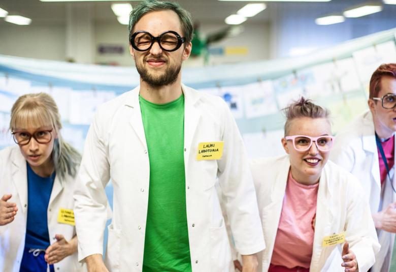 Kuvassa on neljä näyttelijää Laura Ikonen, Aleksi Kinnunen, Anna-Maria Vänskä ja Janne Puustinen ja he ovat valkoisissa takeissa kävelemässä eteenpäin. 