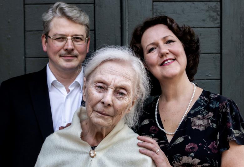 Kuvassa on vasemmalla takana Jyrki Attila, jolla on harmaat, kihartuneet hiukset päälaella ja silmälasit. Oikealla takana Pia Freund on pää vinosti ja hänellä on tummat hiukset taivutettuna taakse.  Edessä on Seela Sella on vaaleat hiukset ja vaalea iso huivi olkapäillään. 