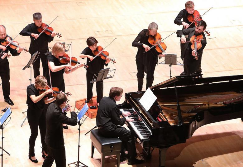 Kuvassa on PianoEspoon esiintyjiä flyygelin takana puolikaaressa soittamassa. Lavalla on puulattia.