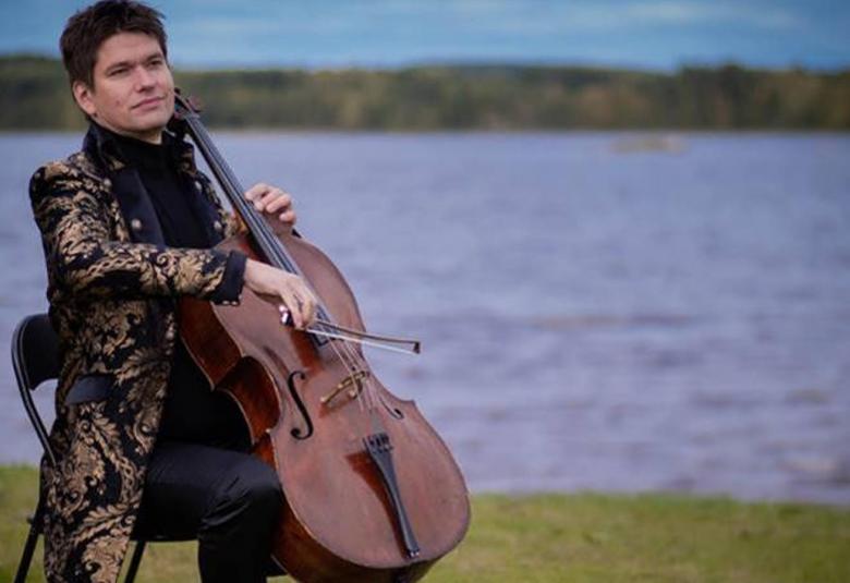 Kuvassa on Jussi Makkonen soittamassa selloa taustallaan järvimaisema ja vapaa, pienesti aaltoileva vesi.