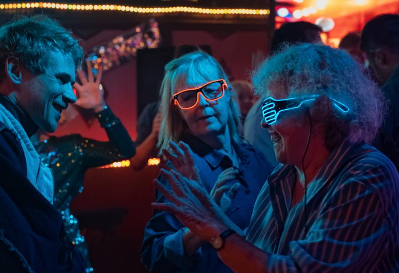 Kuvassa on leidit Leena Uotila ja Saara Pakkasvirta pimeähkössä tilassa led-laseissa ja he keskustelevat intensiivisesti vasemmalla seisovan Samuli Niittymäen kanssa.  