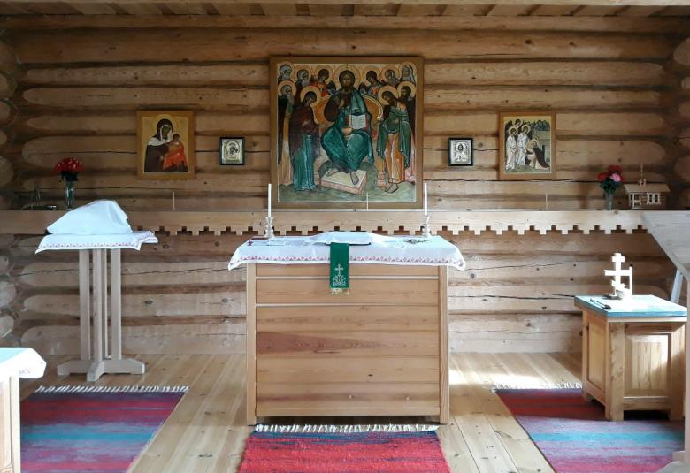 Kuvassa on Kaavin tsasounan sisätila, jossa on hirsisessä rakennuksessa  puukalusteet sekä puinen alttari keskellä.  Seinällä on ikoneita ja suurin keskellä.