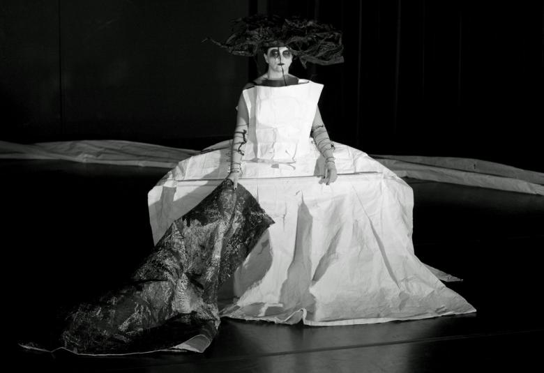 Kuvassa on Pirjo Valinen valkoisessa pitkässä paperipuvussa.  Puvussa on vasemmassa sivussa harmaa laahus. Kuva on musta-valkoinen.