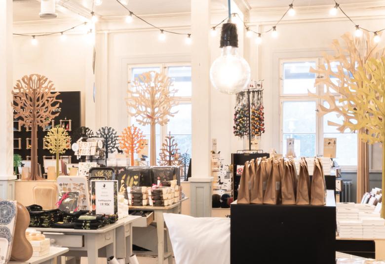 Kuvassa on Oulun Taito-shop -myymälä ja siinä on esillä erilaisia käsityötuotteita sekä puusta tehtyjä puita. Myymälä on kauniisti valaistu ja ilmeeltään valoisa.   