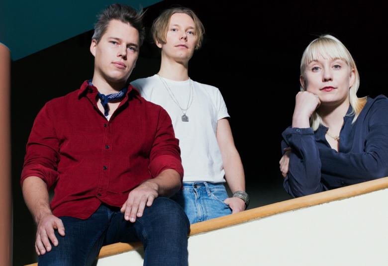 Kuvassa on Amos Rexin Between us -näyttelyn taiteilijat Tero Kuitunen, Raimo Saarinen ja Karoliina Hellberg. Heidät on kuvattu alhaalta ylöspäin nojaamassa kaiteeseen.