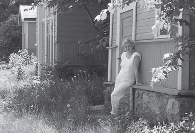 Kuvassa on Laila Hirvisaari Lappeenrannan linnoituksen puutalon pihalla.  Kuva on musta-valkoinen.