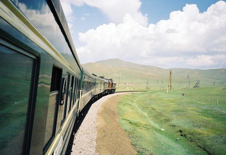 Kuvassa on vihreä Siperian juna, joka kaartaa pitkin raidetta siperialaisessa maisemassa.