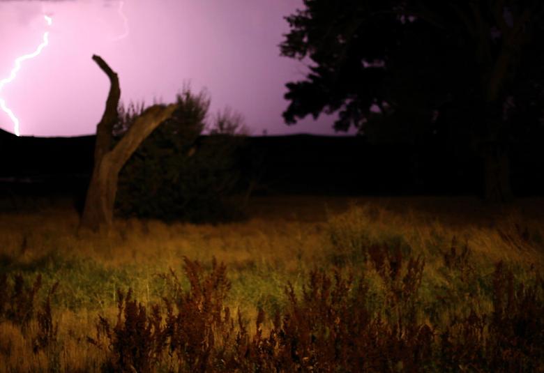 Kuvassa on tumahko maisema, jossa on vasemmalla maahan lyövä salama.