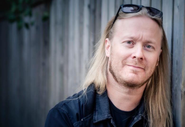 Kuvassa on Antti Hyyrynen, josta on puolivartalokuva.  Hänellä on vaaleat pitkähköt hiukset.