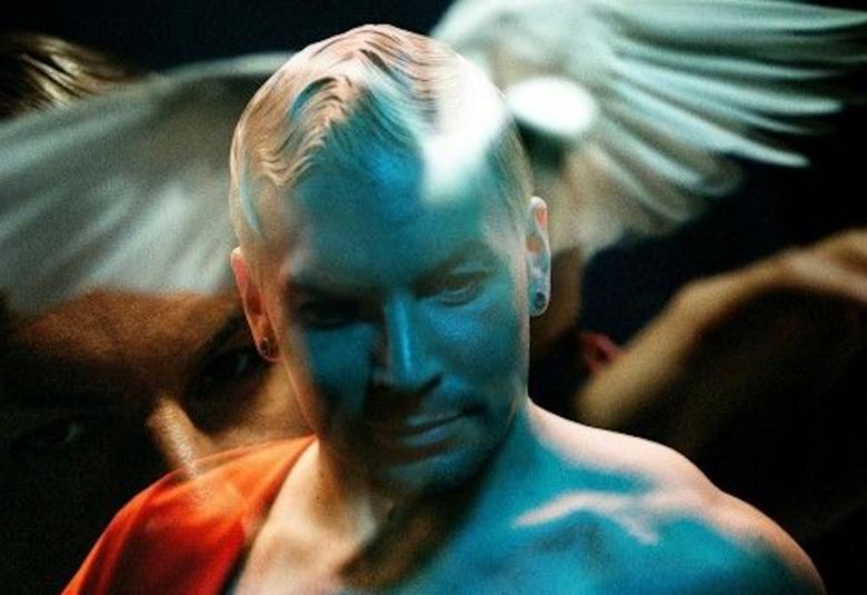 Kuvassa on Antti Tuisku päänsä takana valkoisen kyyhkysen siivet.  Hänellä on paljas rinta ja kuvaa on sävytetty turkoosilla.  Ympärillä on ruskeita käsiä ja jalkoja.