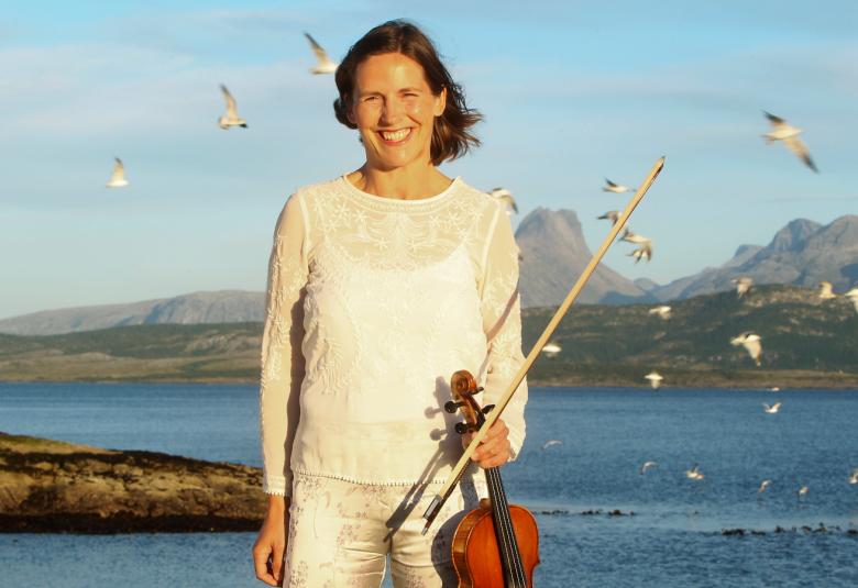 Kuvassa on Cecilia Zilliacus, joka seisoo meren äärellä.  Takana on merimaisema, jossa lentelee lokkeja ja taustalla näkyy metsämaisemaa.