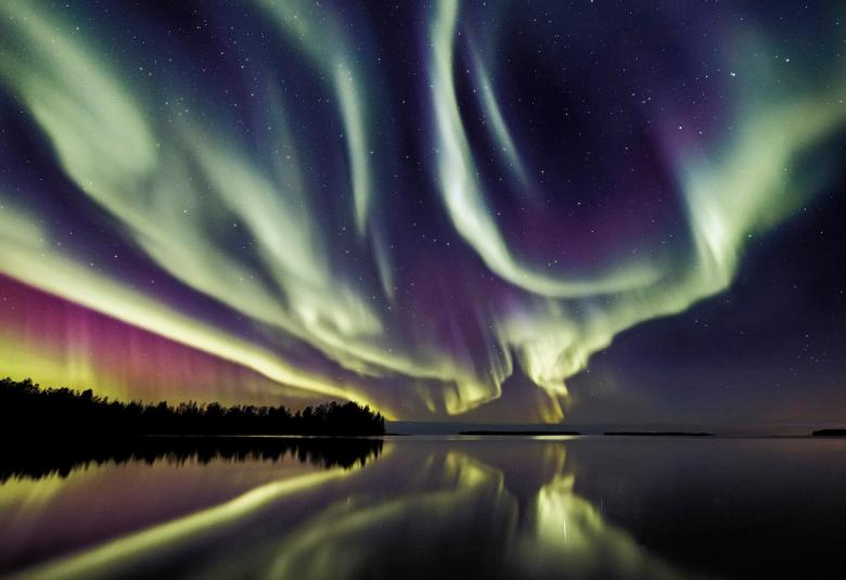 Kuvassa on järvimaisema illalla ja taivalla on värikkäät revontulet.