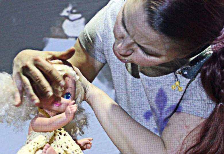 Kuvassa on Kati Keskihannu, joka leikkii nukella. Kuvassa näkyy kasvot ja osa nukesta.  