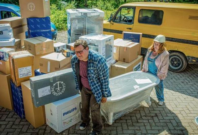 Kuvassa on keltainen pakettiauto ja muuttolaatikoita. Sami Hedberg ja Kiti Kokkonen kantamassa kylpyammetta sisään. 