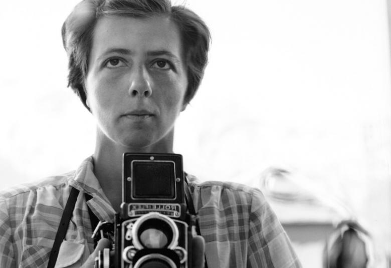 Kuvassa on Vivian Maier kameransa kanssa puolivartalokuvassa. Kuva on musta-valkoinen.