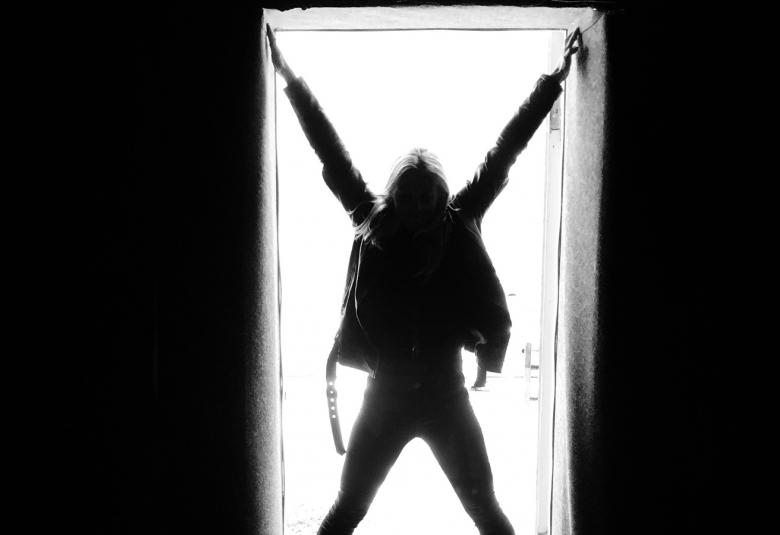 Kuvassa on osa näyttelyn julisteesta, jossa on mustat reunukset ja siinä valkoisella pohjalla ihmisfiguuri, joka on haara-asennossa.