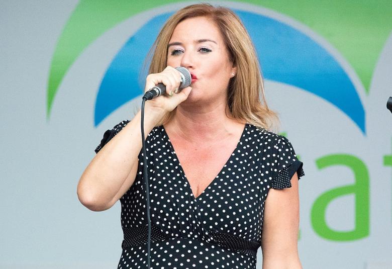 Kuvassa on Milana Misic laulamassa vaalean sinisessä valkopilkullisessa mekossa mikrofoni kädessään.