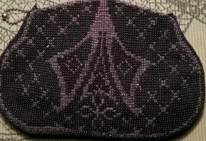 Kuvassa on helmillä päällystetty käsilaukku, jossa on tummia helmiä ja vaaleampia.  Nämä muodostavat koristeellisen kuvion keskelle laukkua. 